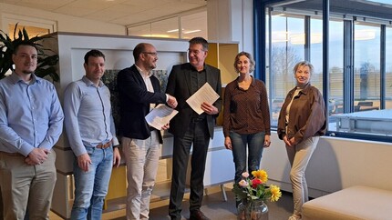 Zes mensen staan op een rij, de middelste twee schudden elkaar de hand en hebben een contract in hun andere hand.