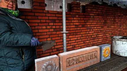 Mevrouw met help om staat klaar om stenen met de tekst "zonnebloem" en twee zonnebloemen in een muur te metselen